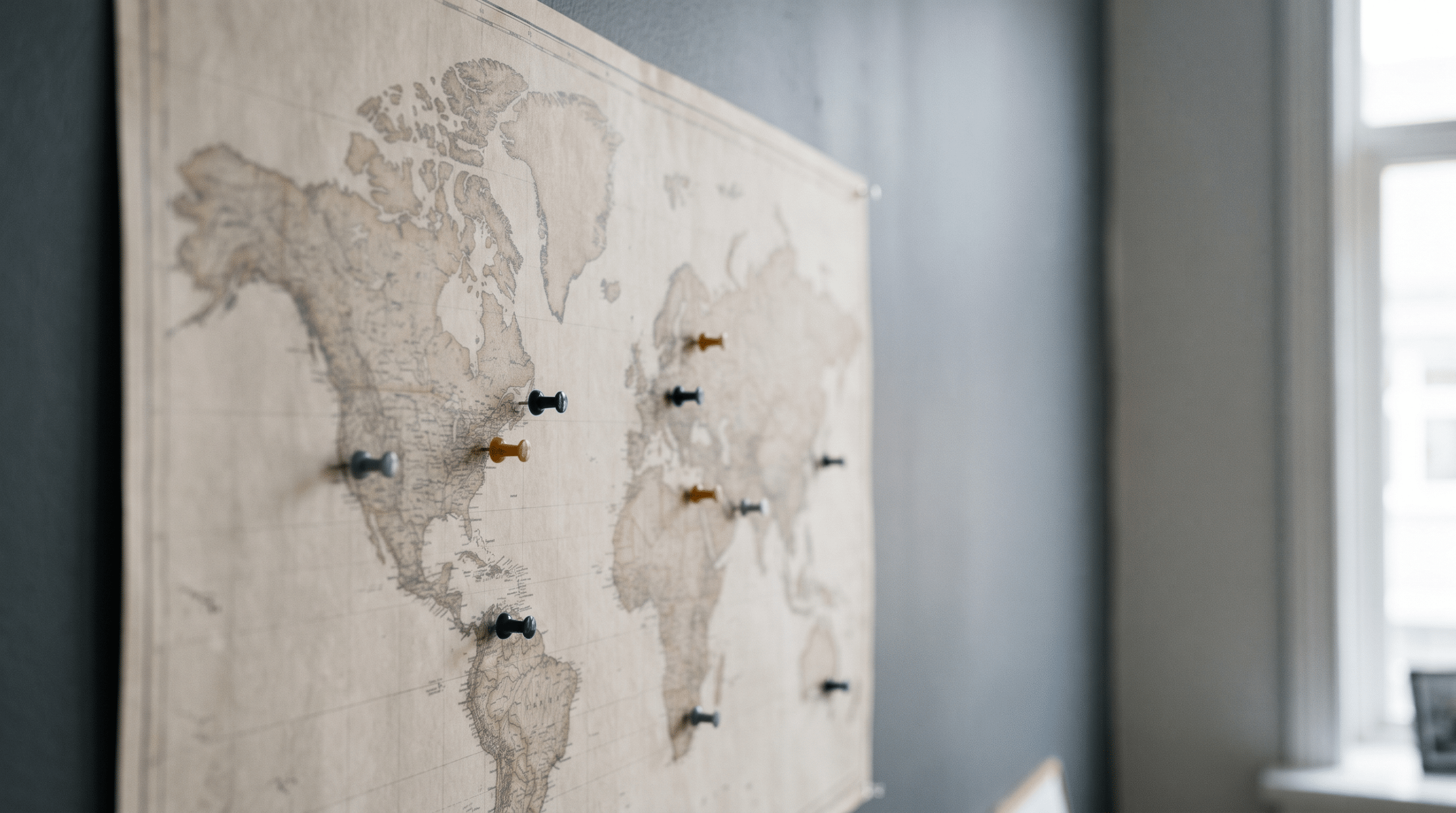 A paper wall map with several small coloured pins pushed into scattered points across it